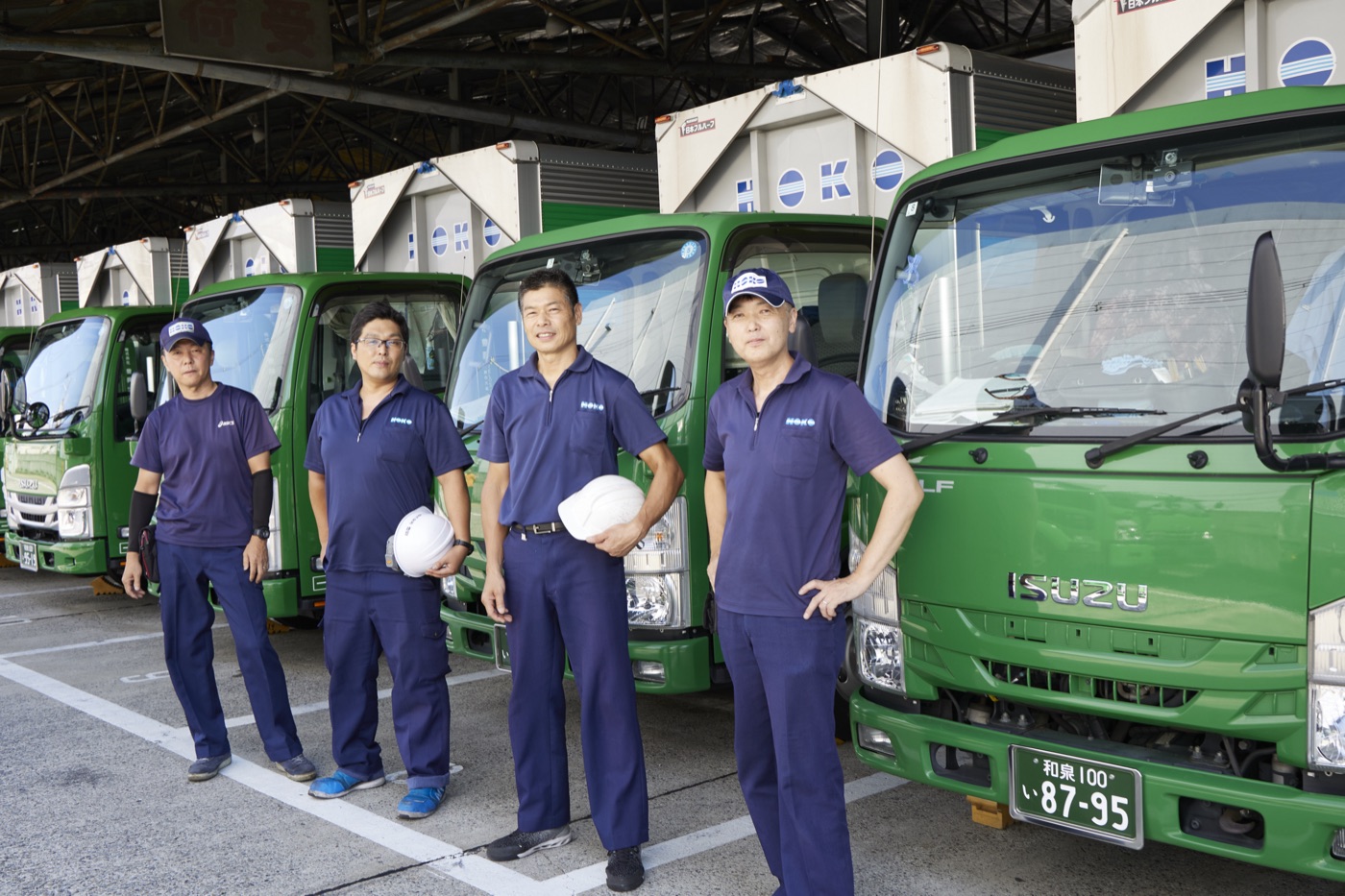 自社センターに並ぶ緑のトラックとドライバー(自社スタッフ)