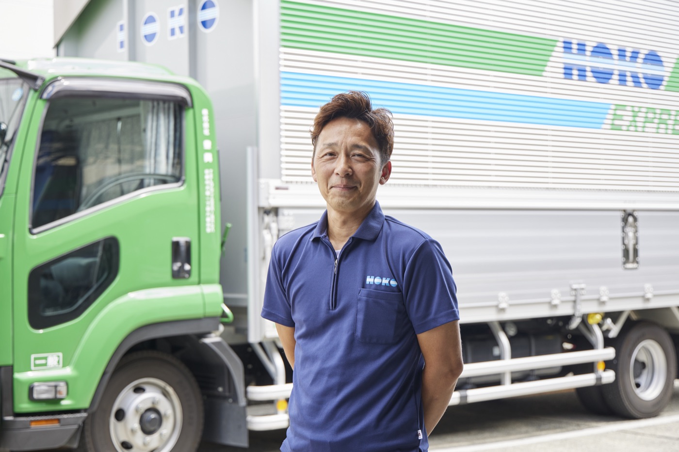 緑のトラックの前に立つHOKOのドライバー（自社スタッフ）