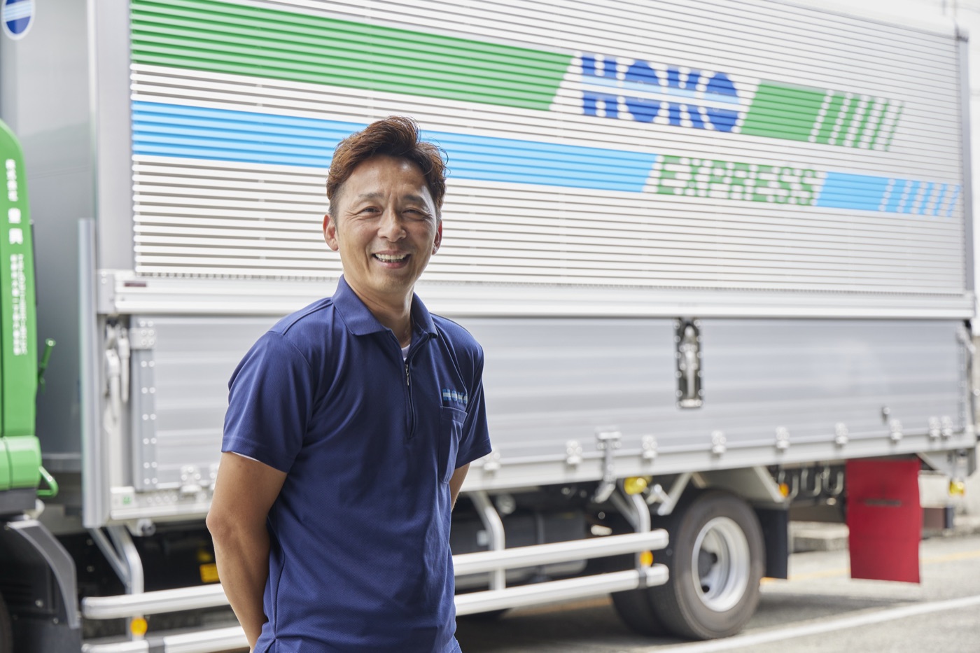 HOKO EXPRESSの車両の前で笑顔のドライバー（自社スタッフ）